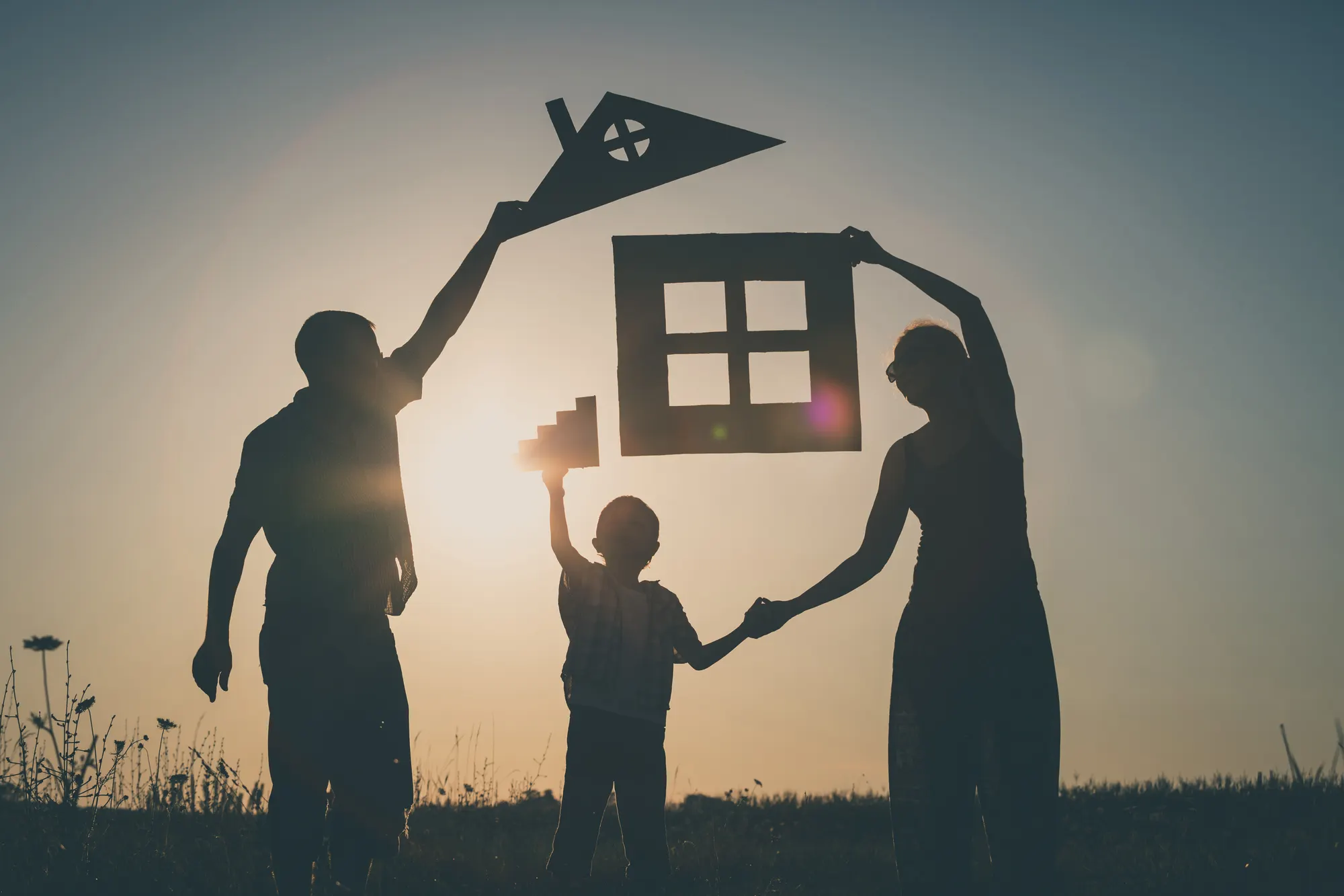 Silhouette of a family at sunset holding up a cutout of a house