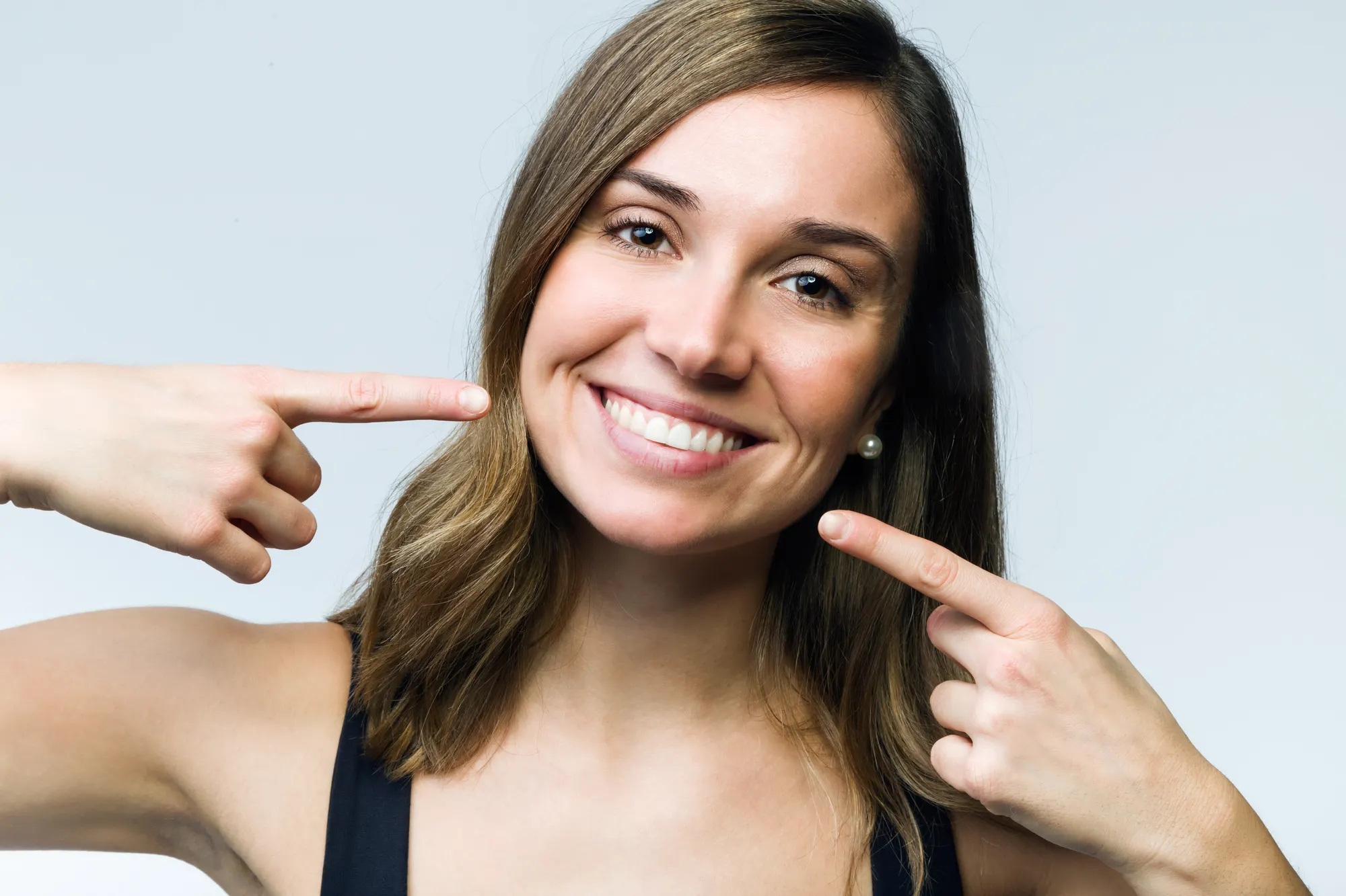 A smiling woman pointing to her teeth against a light background