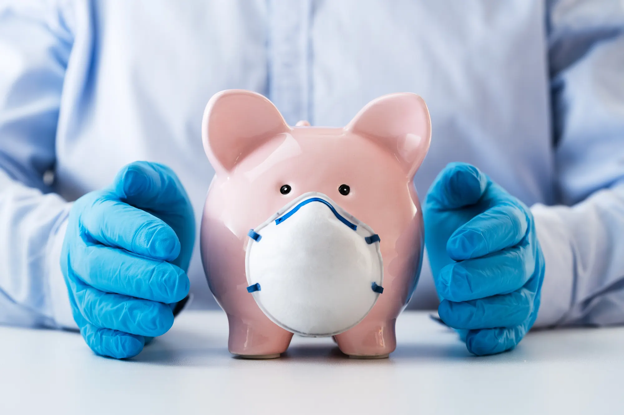 Gloved hands cupped around a piggy bank wearing a face mask