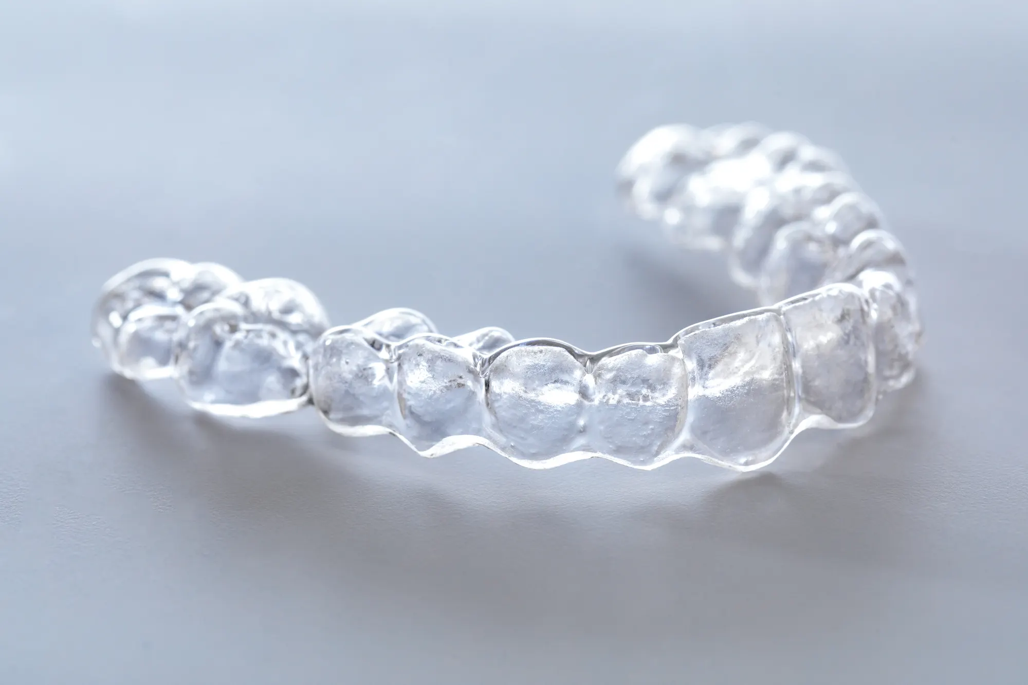 A clear plastic aligner resting on a gray surface