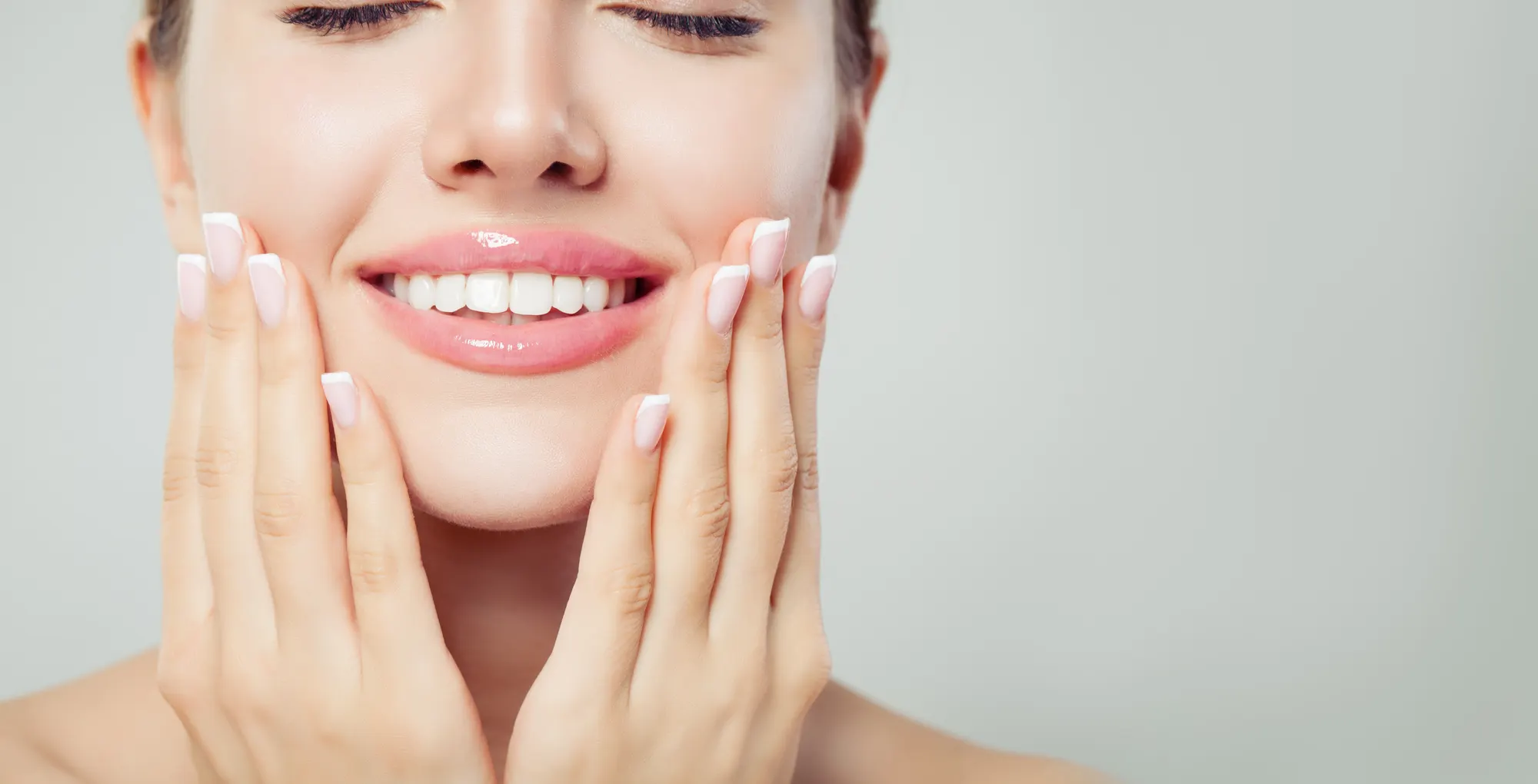 A close-up of a smiling woman with her hands framing her face